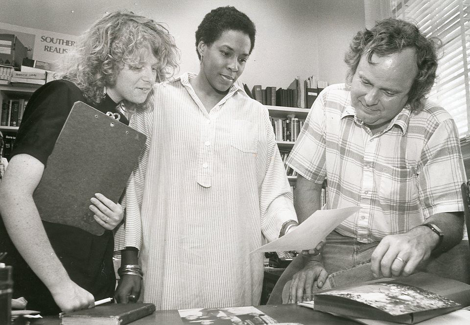 A black woman, Maryemma Graham, standing between a white man and woman, looking at papers in her hand.